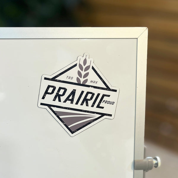 A die-cut magnet with the text 'PRAIRIE PROUD' on it, placed on a white surface.
