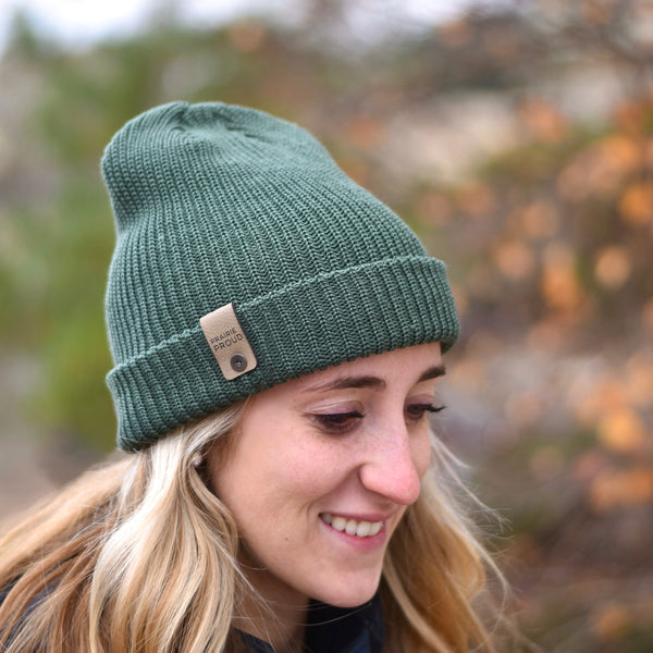 A woman wearing a green knit beanie with a leather clip label.