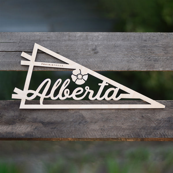 A wooden pennant with the word 'Alberta' printed on it, placed on a wooden surface.