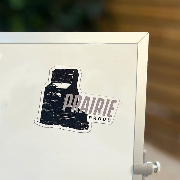 A rectangular magnet with a black and gray design, featuring the silhouette of an elevator and the text 'PRAIRIE PROUD'.