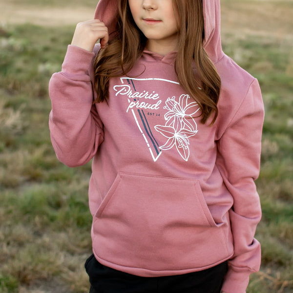 A child wearing a pink hoodie with the text 'Prairie Proud' and a floral design on it, in an outdoor setting.