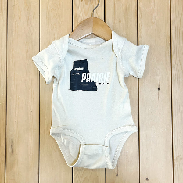 A cream baby onesie with a graphic print on the front displayed on a wooden hanger against a wooden background.