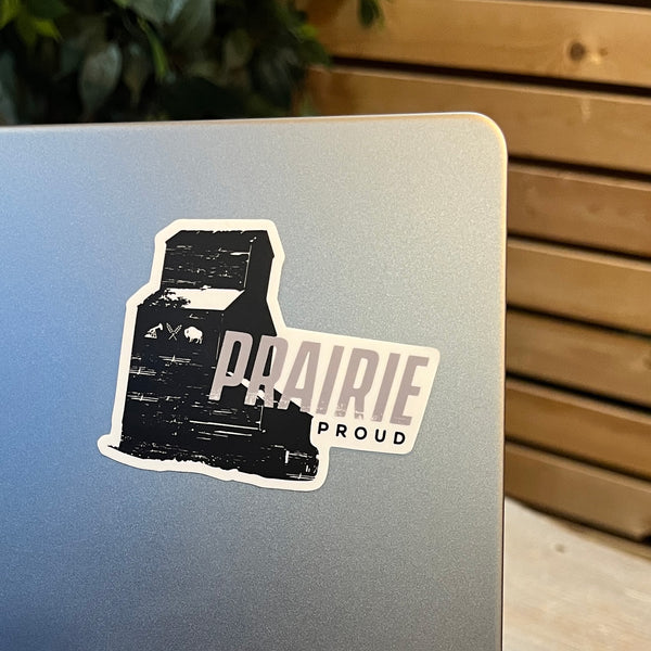 A black and grey die cut vinyl sticker with the silhouette of a grain elevator and the text 'PRAIRIE Proud' placed on a laptop.