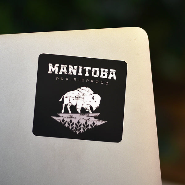 A black and white sticker with the text 'MANITOBA' and an image of a bison, placed on a grey surface.