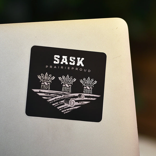 A black and white die cut vinyl sticker with the words 'Sask Prairie Proud' and a graphic of wheat