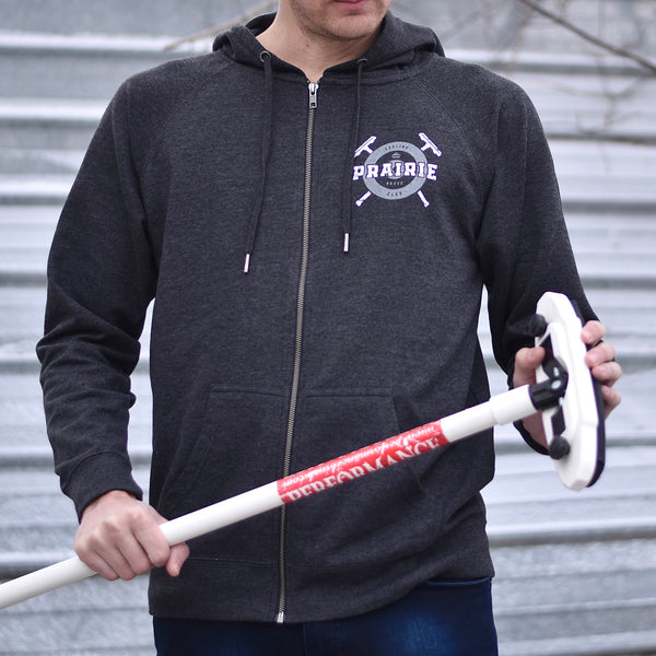 A person wearing a grey zip up hoodie with the text 'prairie proud' and a curling inspired design.