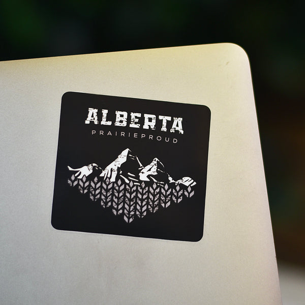A black and white sticker with 'Alberta Prairie Proud' text and a mountain design on it, placed on a laptop.