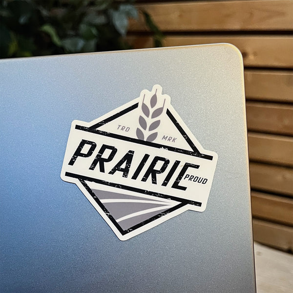 A die cut vinyl sticker with the text 'PRAIRIE PROUD' on it, placed on a laptop.