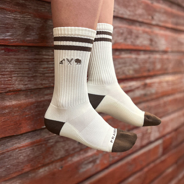 A pair of white and brown padded crew socks with brown icon logo on the outside ankle area.