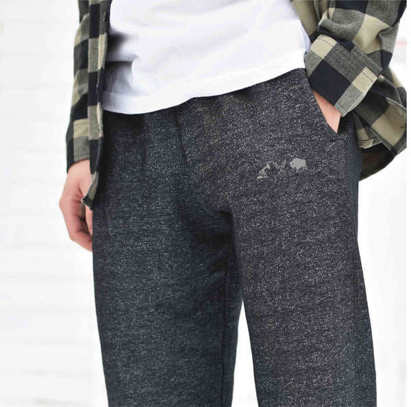 A person wearing heather charcoal sweat pants with a grey icon logo on the left leg.