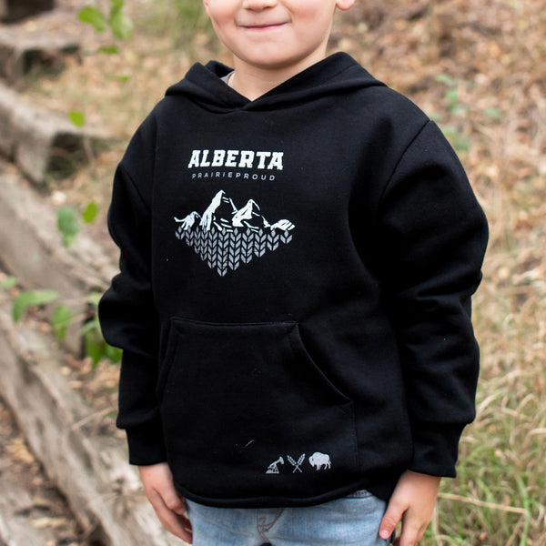 A child wearing a black hoodie with 'Alberta' and 'Prairie Proud' text and a mountain design in white.