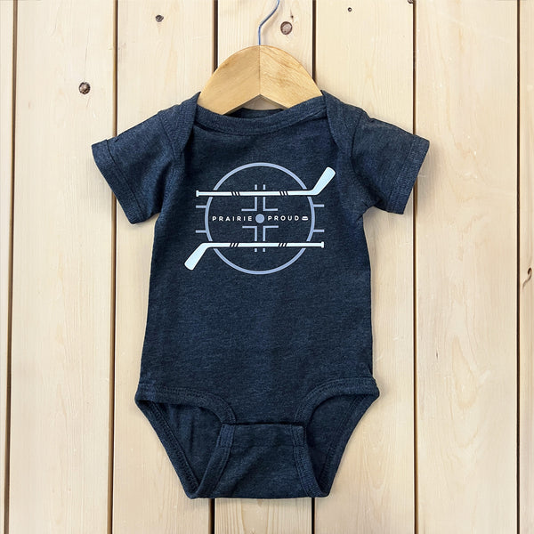 A gray baby onesie with a graphic print of hockey sticks, displayed on a wooden hanger against a wooden background.