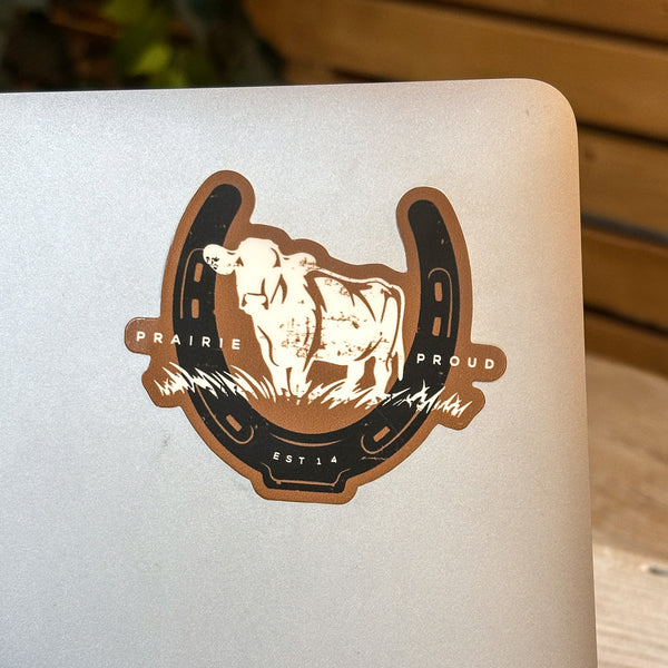 Sticker with a cow design and 'Prairie Proud' text on a white surface.