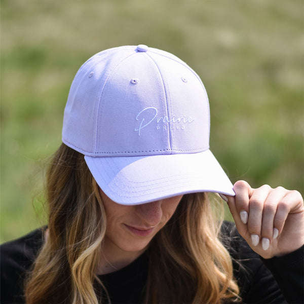 A person wearing a light purple baseball cap with an adjustable slider, featuring a subtle logo with text that says 'prairie proud'.