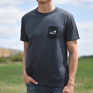 Man wearing a dark grey t-shirt with a black pocket on the top left that says 'prairie proud'.