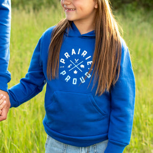 Child wearing a blue 'Prairie Proud' hoodie in a grassy field