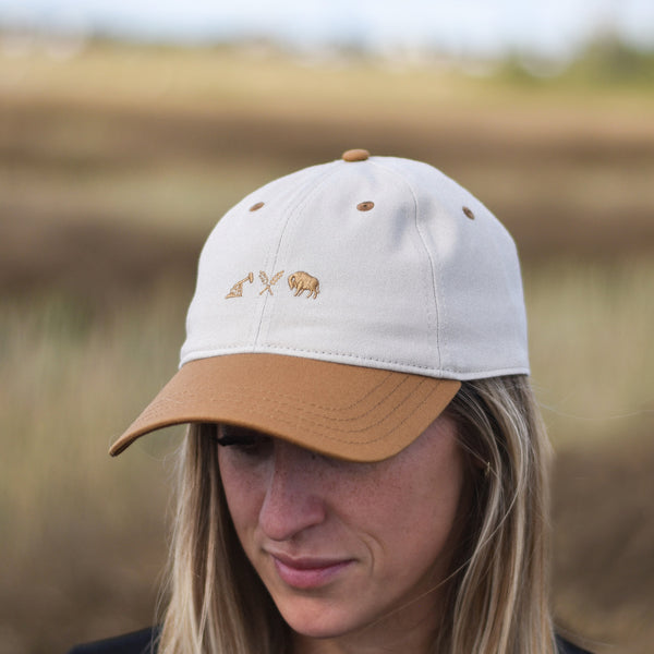 A hat with a caramel brim and white crown, with a caramel coloured icon logo on the front.