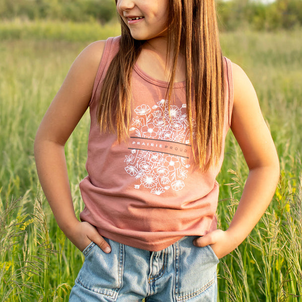 Young girl wearing a pink tank top with floral design in a grassy field