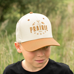 Child wearing a Carmel and Cream coloured cap with 'Prairie Proud' text in a natural setting