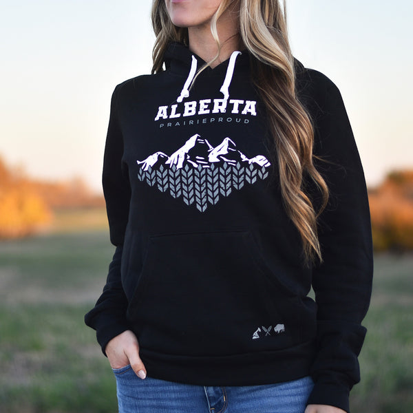 A person wearing a black hoodie with 'Alberta Prairie Proud' and mountain range graphic in white.