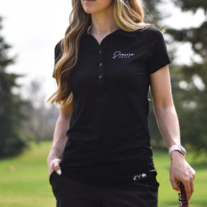 A female model wearing a black athletic polo shirt with left chest embroidery that says 'prairie proud'.