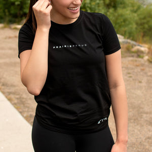 A female model wearing a black athletic crew t-shirt with the text 'PRAIRIE PROUD' across the chest.