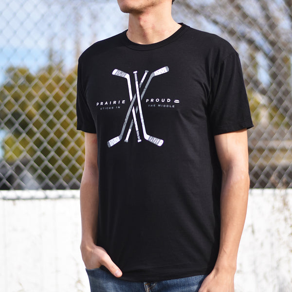 A person wearing a black crew t-shirt with a graphic of hockey sticks and the text 'PRAIRIE PROUD'.