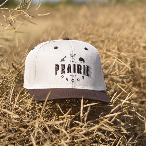 A snapback hat with a brown brim and a white crown, with brown text that says 'Prairie Proud'.