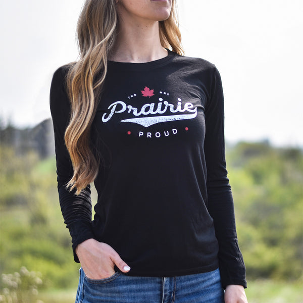 A female model wearing a long sleeve black crew t-shirt with the text 'Prairie Proud' in a baseball inspired design.