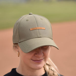 A person wearing a green baseball cap with an adjustable slider and a tan suede patch on the front.