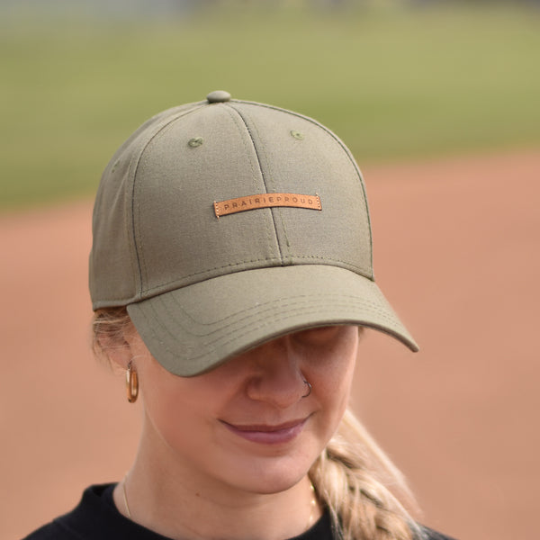 A person wearing a green baseball cap with an adjustable slider and a tan suede patch on the front.