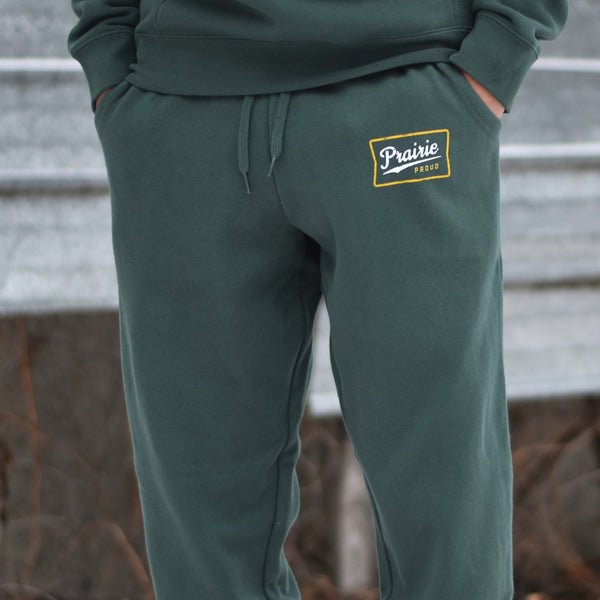 A person wearing green unisex retro joggers with the text 'Prairie Proud' on the left hip.