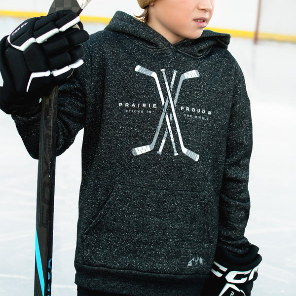 A child wearing a heather charcoal hoodie with 'Prairie Proud' and hockey stick graphics on the front, holding a hockey stick.