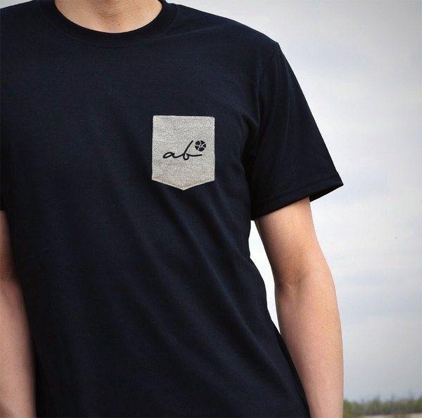 Man wearing a black t-shirt with a grey pocket on the top left that says 'ab' (Alberta).