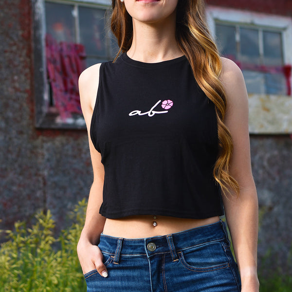 A woman wearing a black crop tank top with the logo 'ab' (Alberta) printed on the front with a small pink flower.