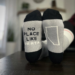 A pair of black and grey crew socks with text 'NO PLACE LIKE BERTA' on the right sock, and the province shape on the left.