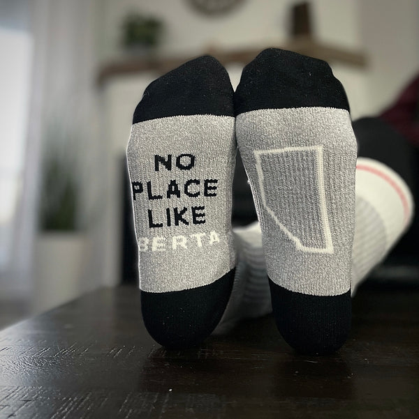 A pair of black and grey crew socks with text 'NO PLACE LIKE BERTA' on the right sock, and the province shape on the left.