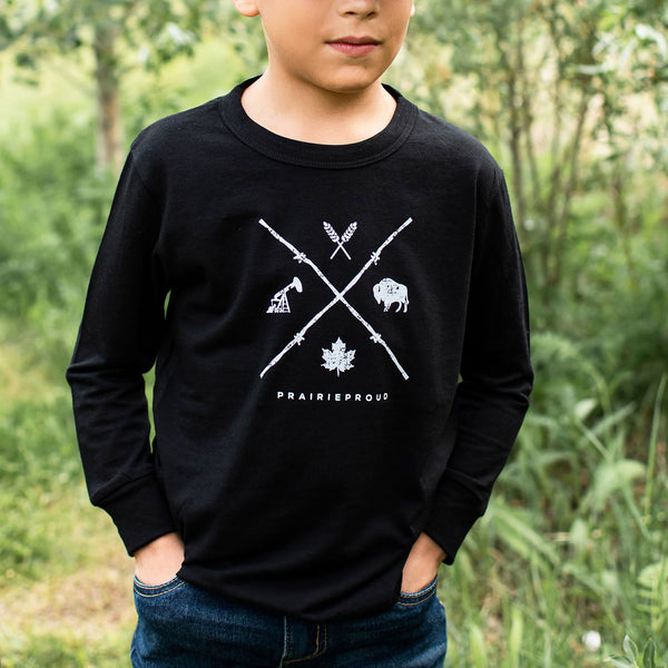 A child wearing a long sleeve black crew t-shirt with a graphic design in white, standing outdoors.