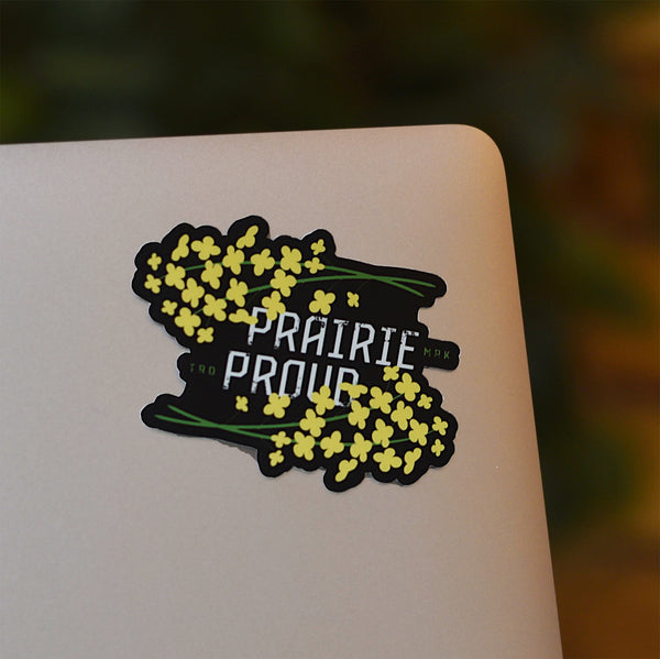 A die cut vinyl sticker with yellow floral pattern and the text 'Prairie Proud' on it, placed on a laptop.