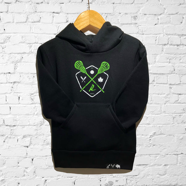 A black hoodie with a graphic design of lacrosse sticks and a shield, displayed on a hanger against a white brick wall.