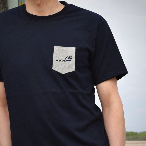 Man wearing a black t-shirt with a grey pocket on the top left that says 'mb' (Manitoba).