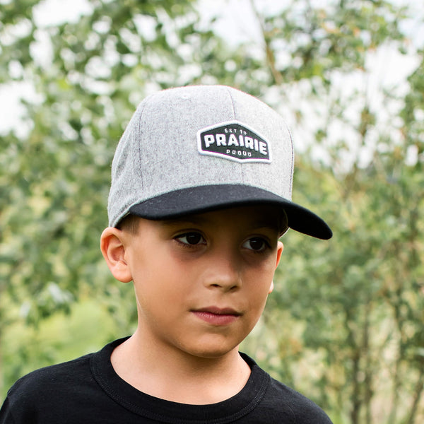 A child wearing a gray and black snapback hat with the text 'PRAIRIE PROUD' on the front.