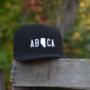 A black flannel snapback hat with 'AB CA' (Alberta Canada) embroidered in white on the front.