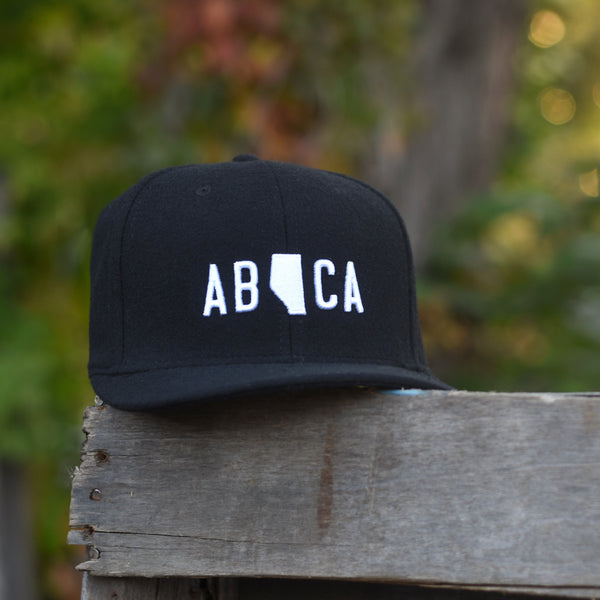 A black flannel snapback hat with 'AB CA' (Alberta Canada) embroidered in white on the front.