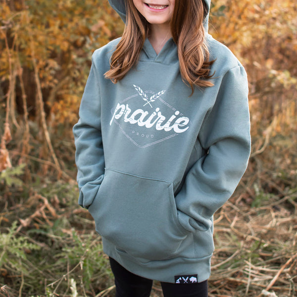 A child wearing a dusty green hoodie with the text 'prairie proud' written across the front in stylized text.