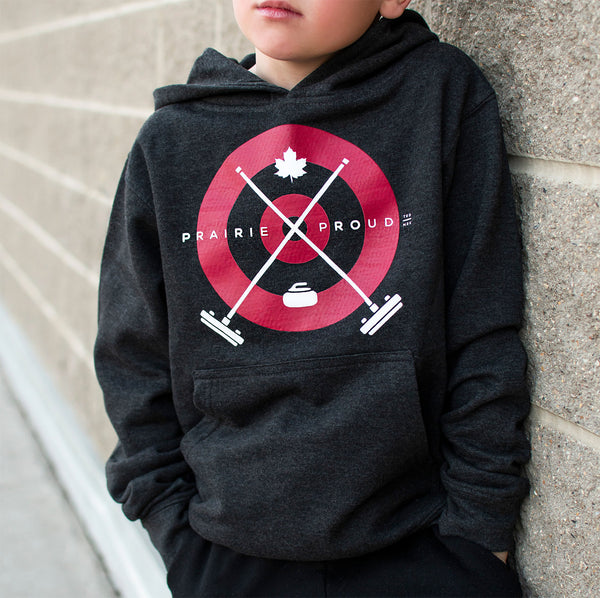 Child wearing a dark heather grey hoodie with a maple leaf, a curling rock and crossed curling brooms over a red print of the house.