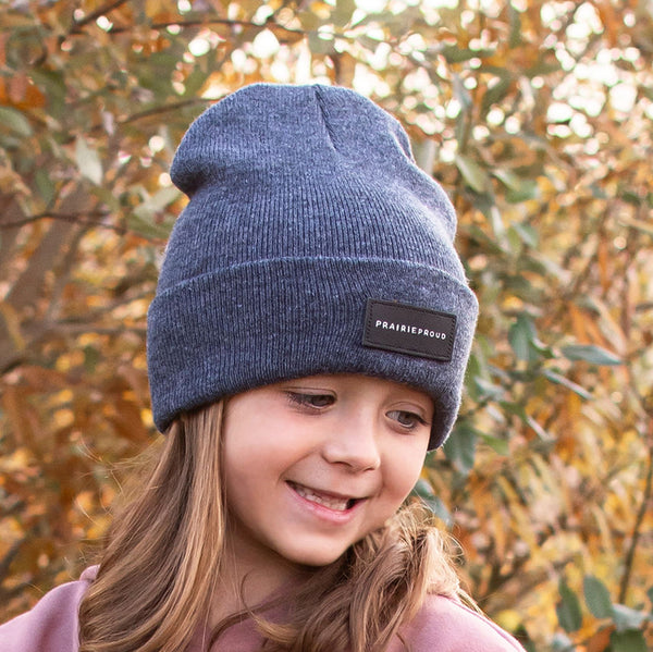 A youth wearing a grey cuffed beanie with a  leather patch on the front.