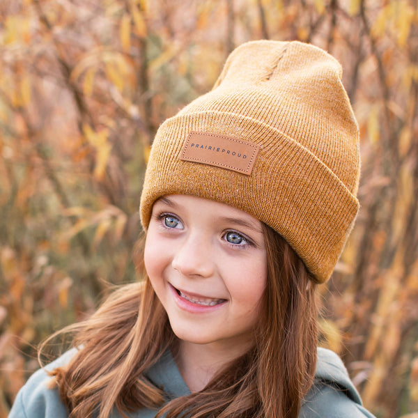 A youth wearing a golden brown cuffed beanie with a  leather patch on the front.