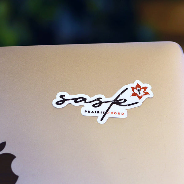 A black and orange die cut vinyl sticker with the words 'Sask' and 'Prairie Proud' on it placed on a laptop.