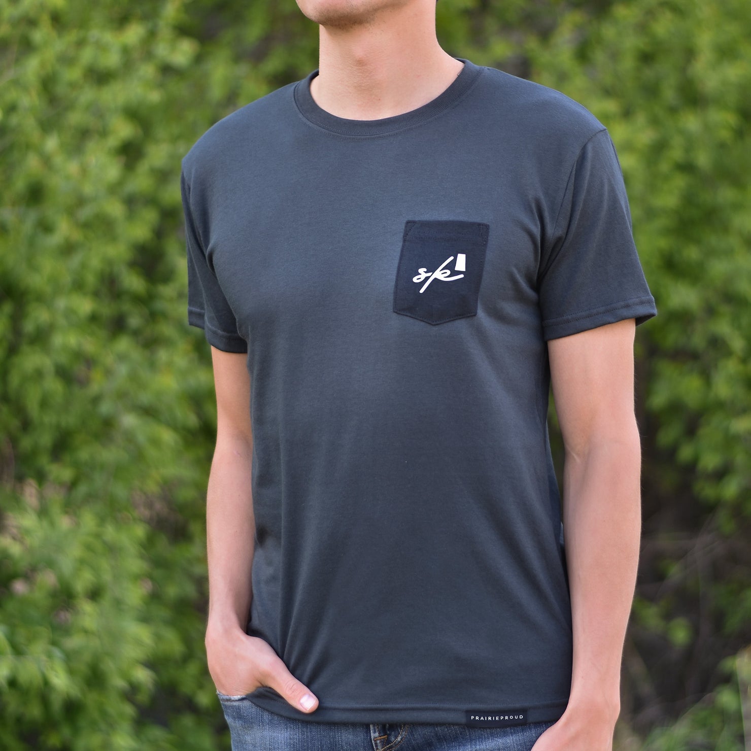 Man wearing a dark grey t-shirt with a black pocket on the top left that says 'sk' (Saskatchewan).